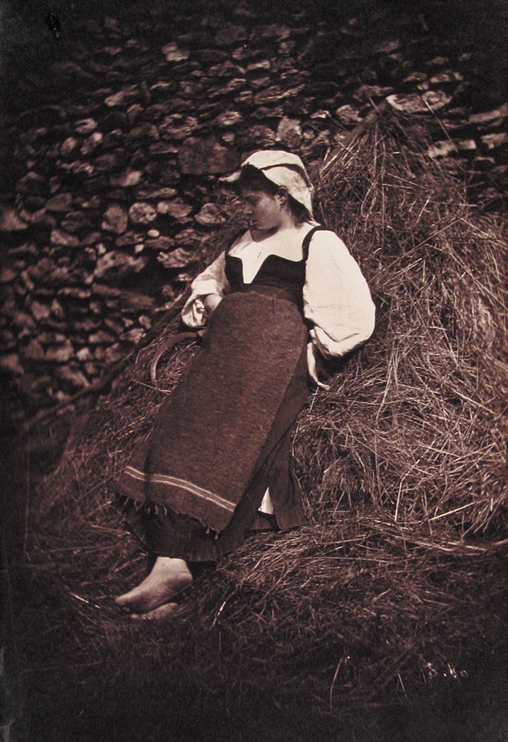 Girl leaning on pile of straw, with scythe